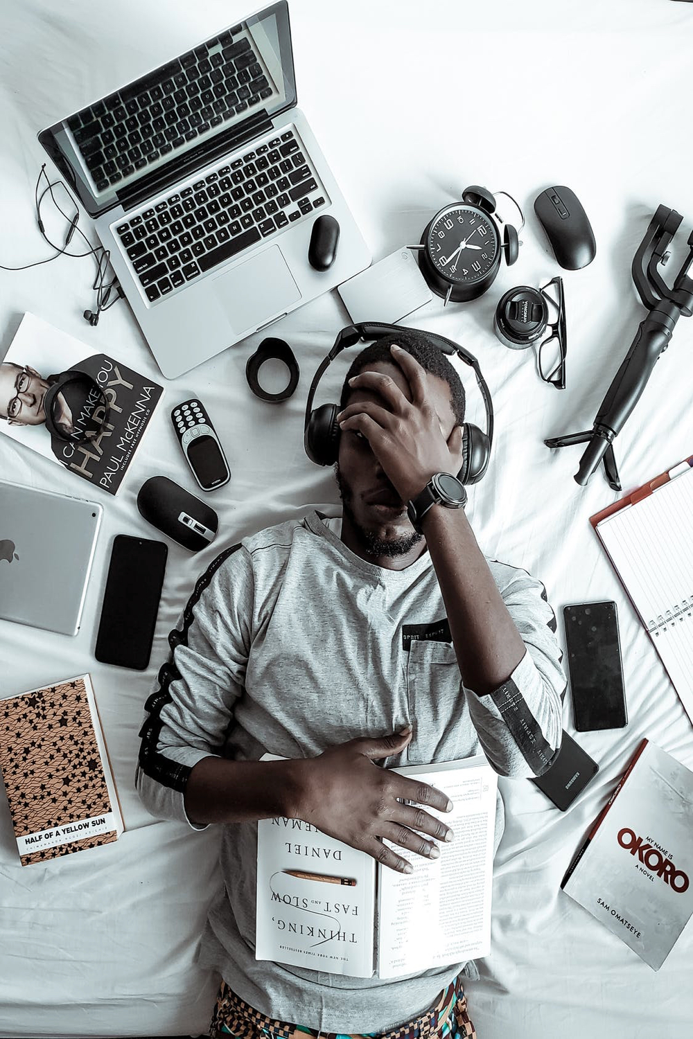 Man lying in bed, surrounded by books and technology